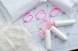 White calendar with pink circles around menstruation date period and clean tampons lying on top.